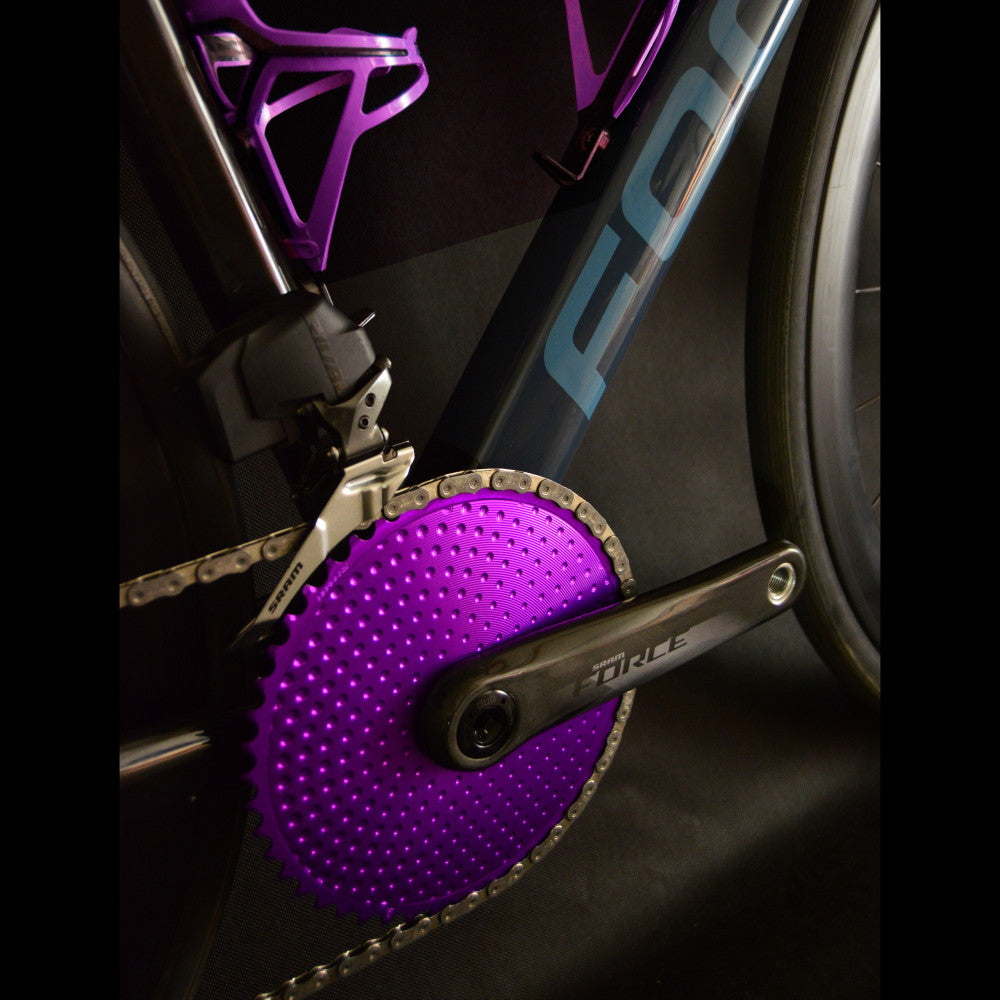 Close-up of purple ALUGEAR round road chainring on SRAM Force crank drivetrain, dark studio lighting