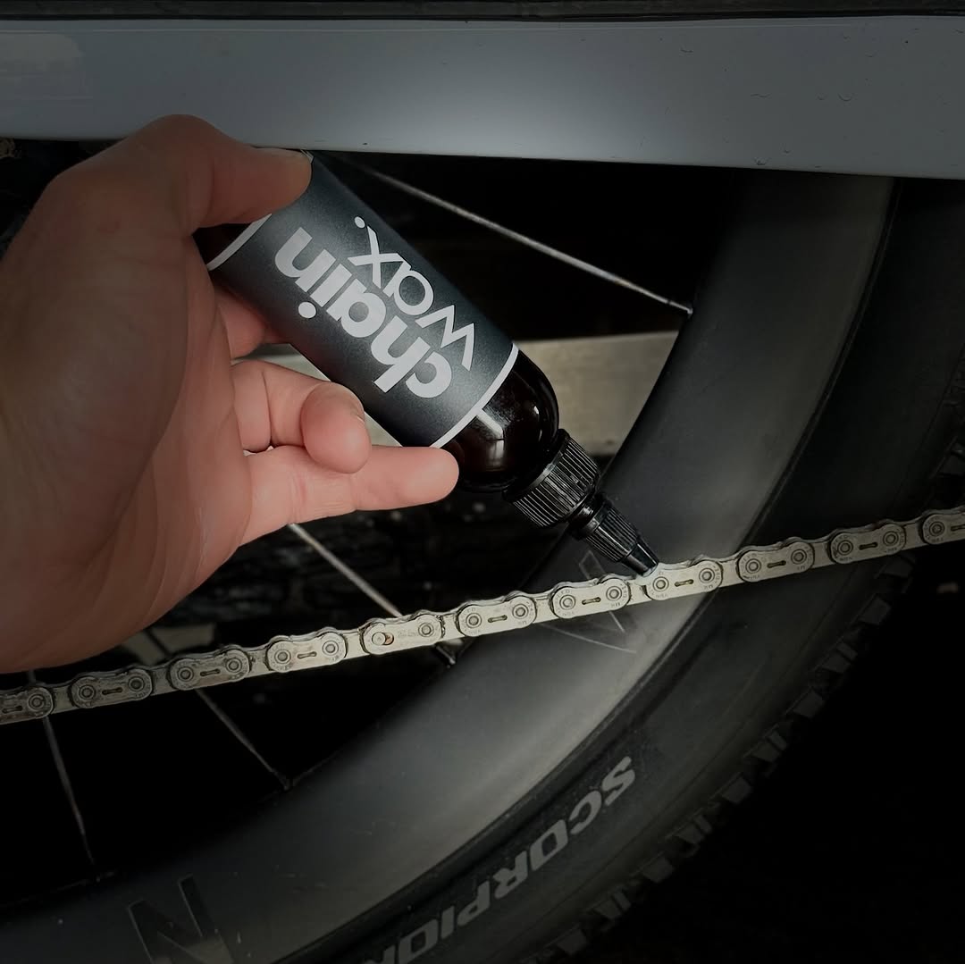 Hand applying ALUGEAR Chain Wax Lube 150ml to bicycle chain near rear wheel